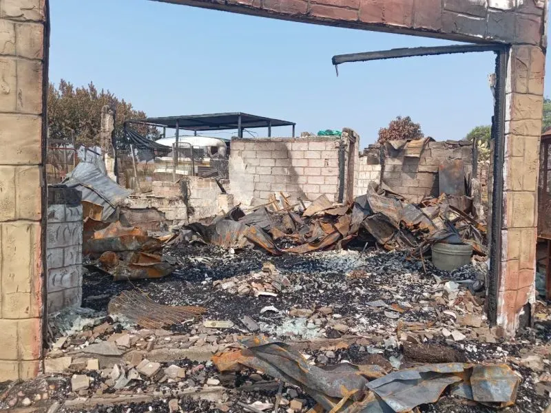 صورة لموقع دمرته النيران، تظهر أنقاض مباني مهدمة ومواد محترقة، تعكس آثار العنف في جنوب أفريقيا وتأثيره على المجتمعات.