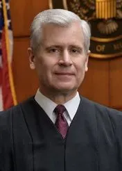 القاضي باتريك شيلتز، يرتدي رداء القضاة، يظهر في قاعة المحكمة، حيث يتناول قضايا الهجرة والامتثال لأوامر المحكمة.