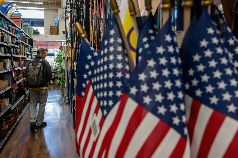 رجل يسير في ممر متجر، محاط بأعلام أمريكية صغيرة، تعكس مشاعر عدم اليقين الاقتصادي في الولايات المتحدة.