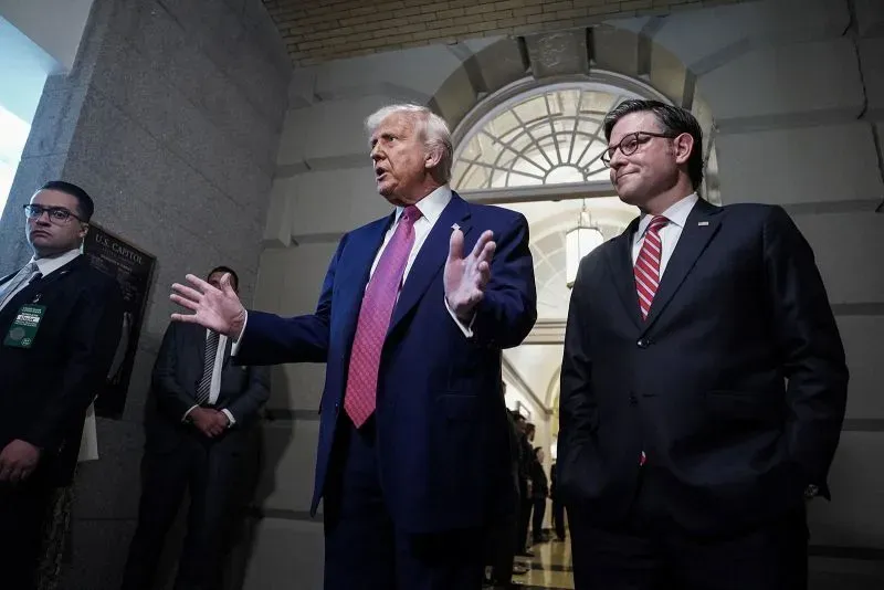 الرئيس ترامب يتحدث في مبنى الكابيتول مع مسؤول حكومي، بينما يظهر أحد الحراس في الخلفية، مما يعكس الأجواء السياسية المتوترة.