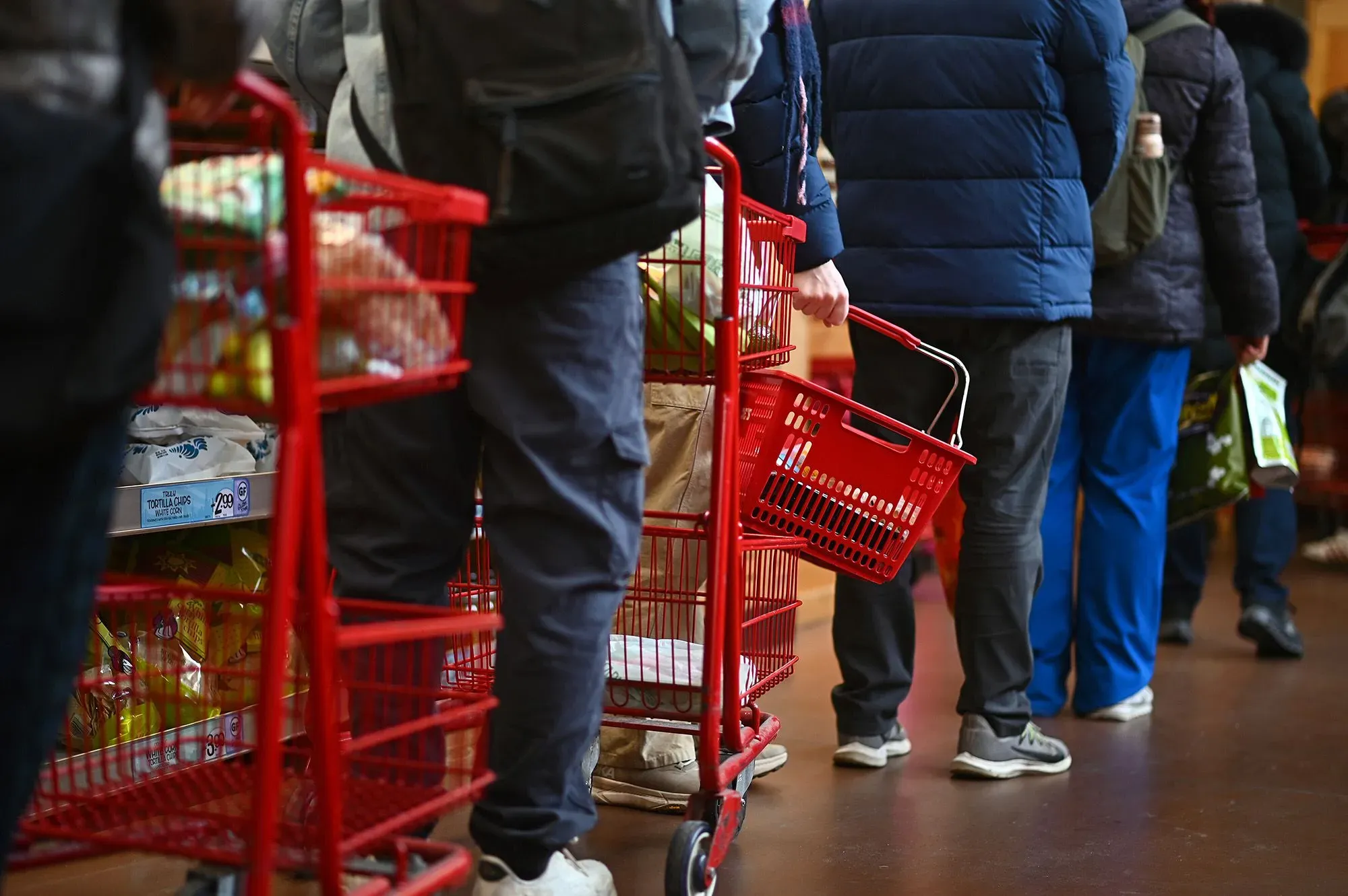 طابور من المتسوقين في سوبرماركت يحملون عربات تسوق حمراء، مما يعكس الضغوط الاقتصادية وارتفاع الأسعار في الولايات المتحدة.