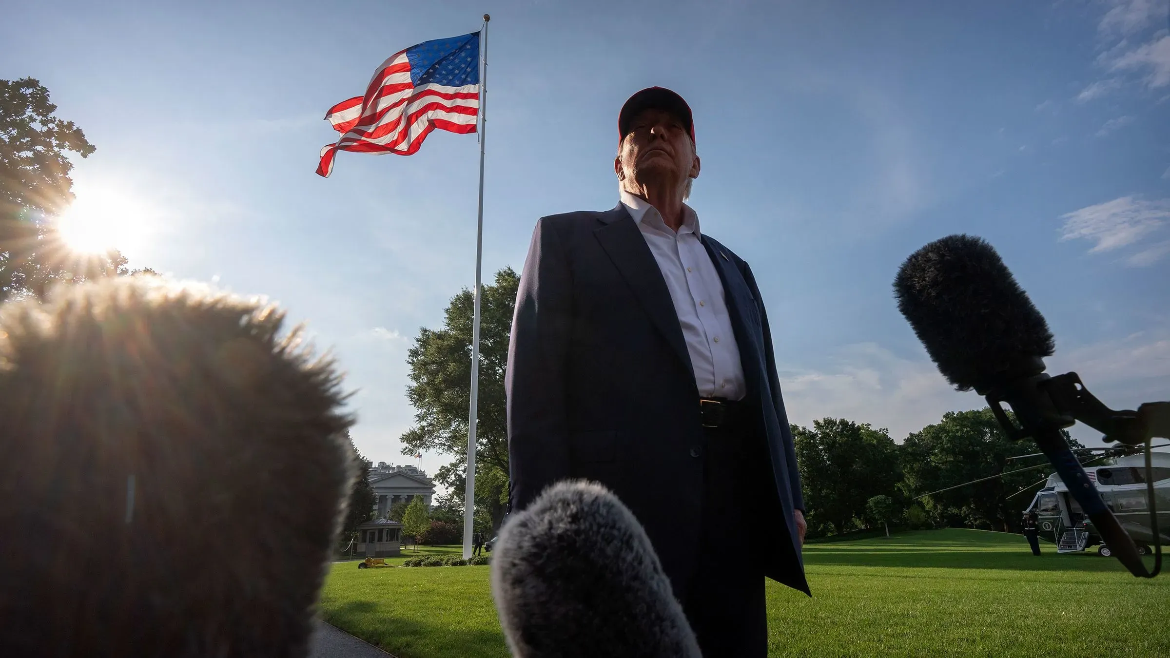 ترامب يقف أمام علم الولايات المتحدة، محاطًا بميكروفونات، مع خلفية مشمسة توضح أهمية اللحظة في سياق إنجازاته التشريعية.