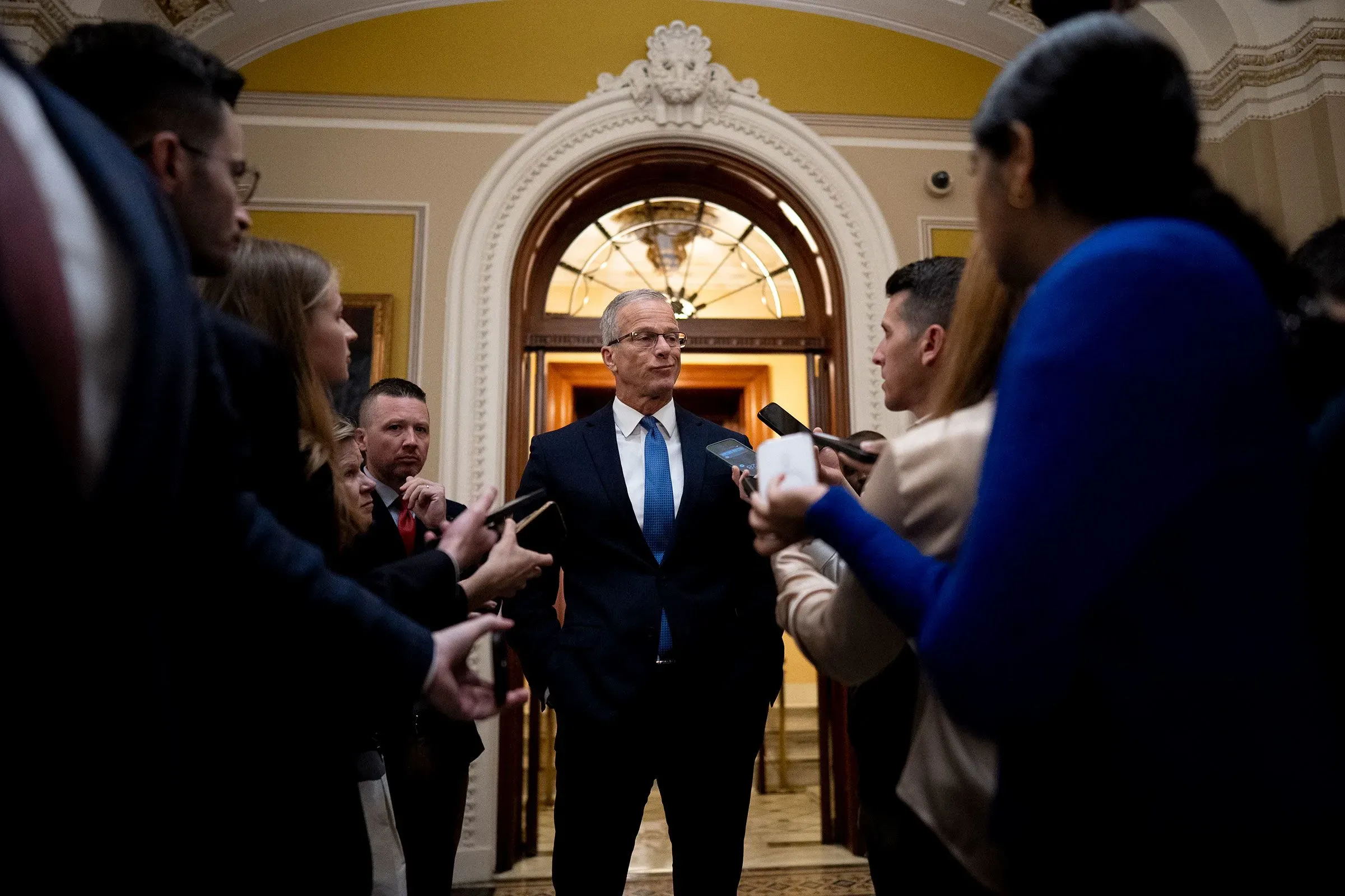 رجل يرتدي بدلة يتحدث مع مجموعة من الصحفيين في مبنى الكونغرس، وسط أجواء توتر حول تمويل وزارة الأمن الداخلي.