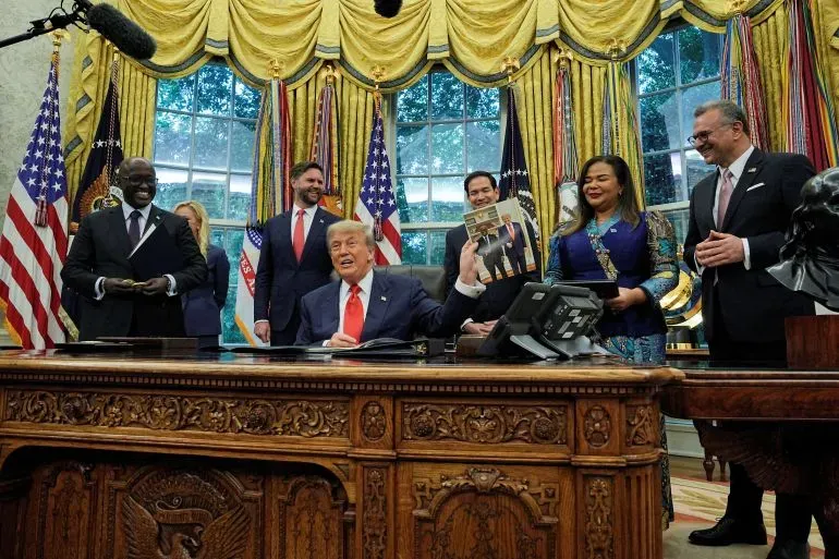 اجتماع في المكتب البيضاوي حيث يظهر ترامب مبتسمًا وهو يحمل مجلة، محاطًا بمجموعة من المسؤولين. يعكس الصورة سياسة الهجرة المثيرة للجدل.