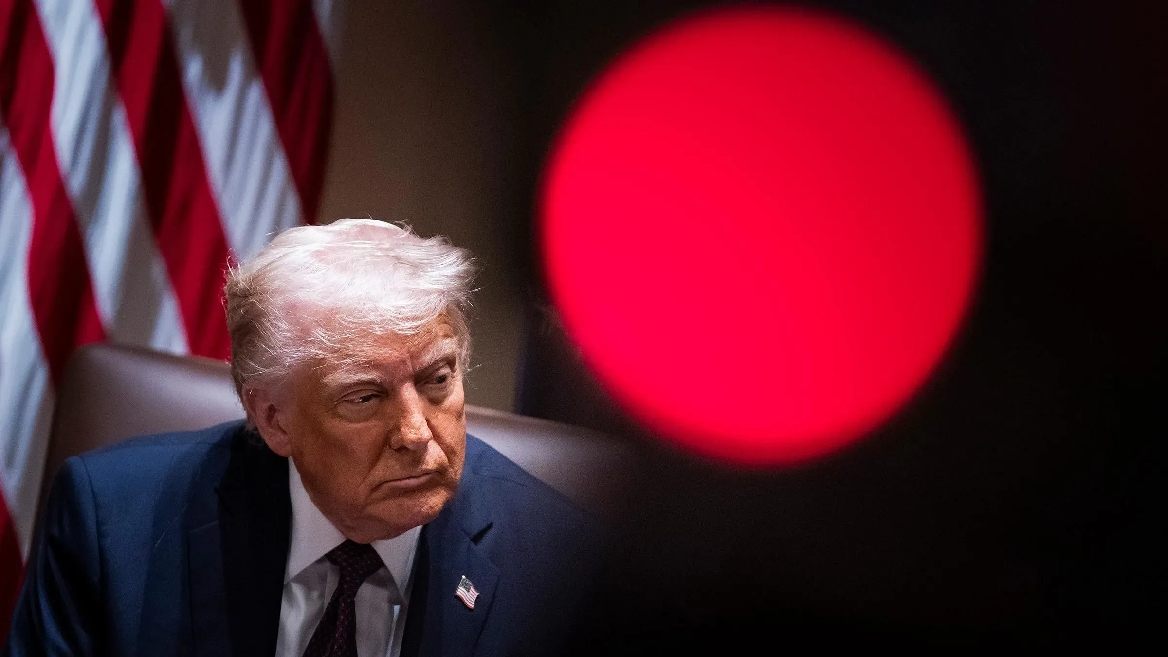 ترامب يجلس في اجتماع، مع العلم الأمريكي خلفه، ويظهر تعبيره الجاد أثناء مناقشة الترشح لولاية ثالثة.