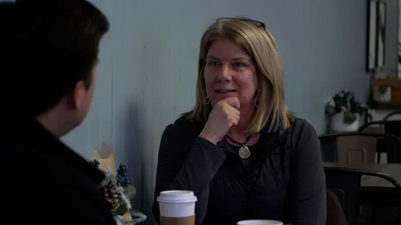 امرأة تتحدث مع رجل في مقهى، تحمل كوبًا من القهوة، تعبر عن اهتمامها بالقضايا الاقتصادية وتأثيرها على الأسعار.