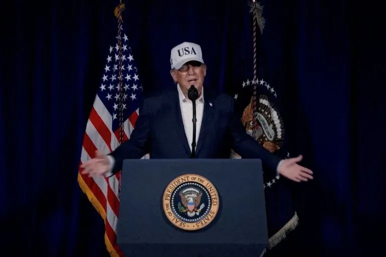 ترامب يتحدث في مؤتمر صحفي مرتديًا قبعة مكتوب عليها "USA"، مع العلم الأمريكي خلفه، مؤكدًا على استمرار العمليات ضد إيران.