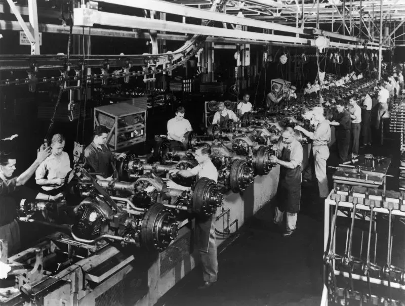 صورة تاريخية لمصنع أمريكي في الخمسينيات، تُظهر عمالاً يعملون على خطوط التجميع، تعكس التغيرات في قطاع التصنيع الأمريكي.