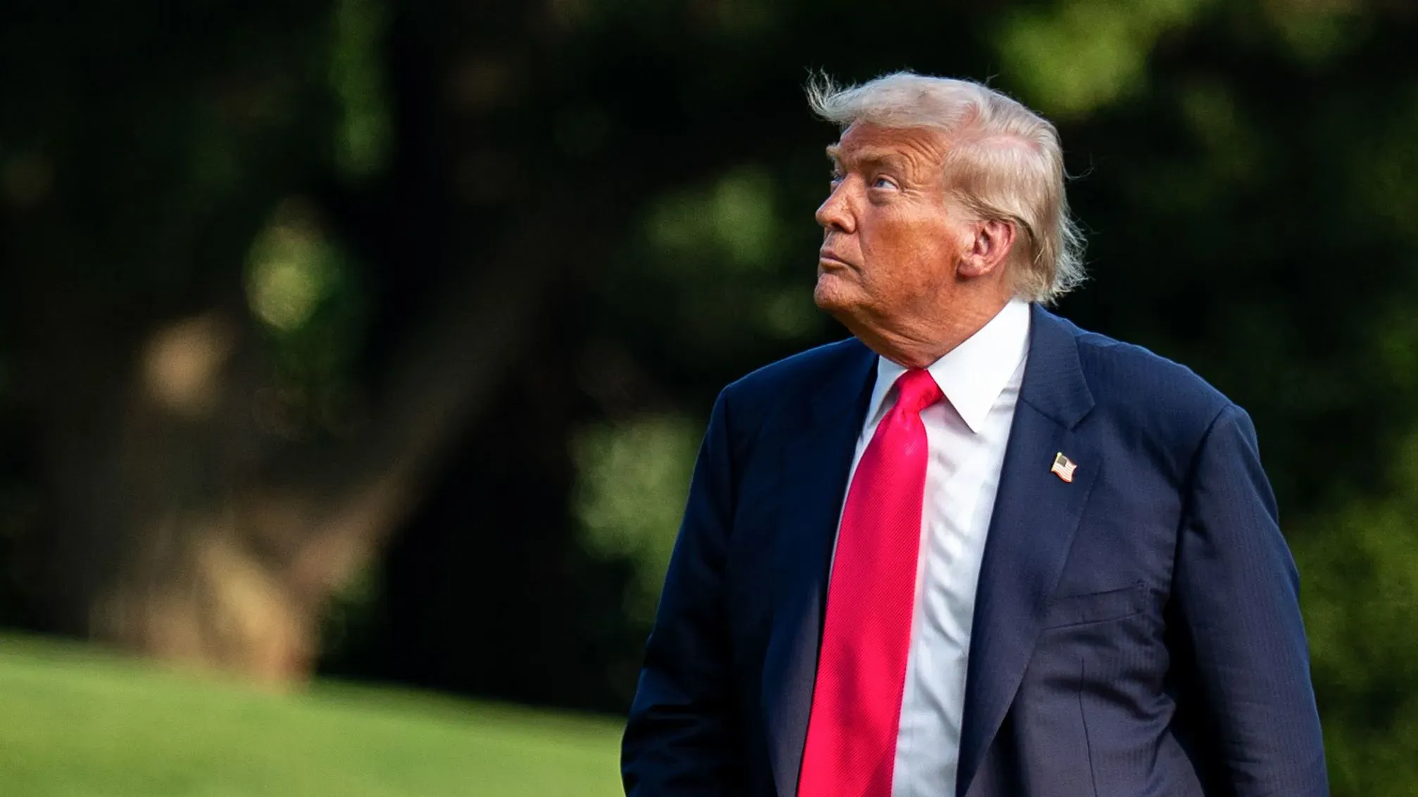 ترامب ينظر إلى الأعلى في حديقة البيت الأبيض، مع تعبير جاد، يعكس توتر الأحداث السياسية الراهنة وتحديات رئاسته.