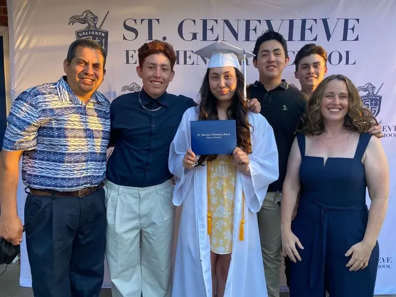 مجموعة من الأشخاص يحتفلون بتخرج فتاة ترتدي قبعة التخرج، مع لافتة تحمل اسم المدرسة "سانت جينيفيف".