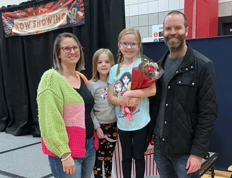 عائلة مكونة من أربعة أفراد، بما في ذلك طفل يحمل باقة من الزهور، في حدث مجتمعي يتناول موضوع التعليم والاختيار المدرسي.