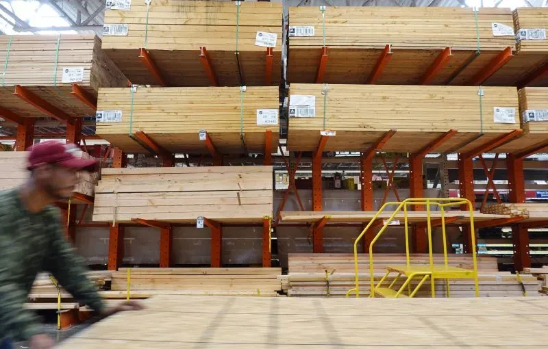 مخازن للأخشاب في متجر، مع رجل يتحرك بالقرب منها. الصورة تعكس تأثير سياسة ترامب على صناعة الأخشاب في الولايات المتحدة.