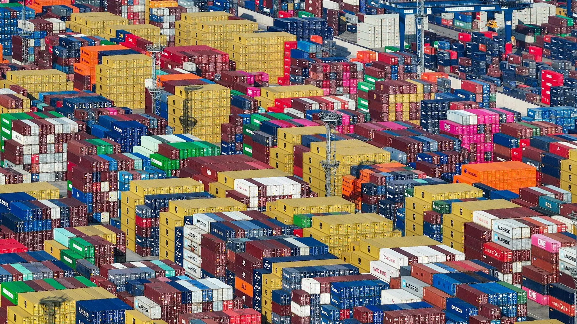 صورة تظهر حاويات شحن ملونة مكدسة في ميناء، تعكس تأثير الحرب التجارية بين الولايات المتحدة والصين على سلسلة التوريد.