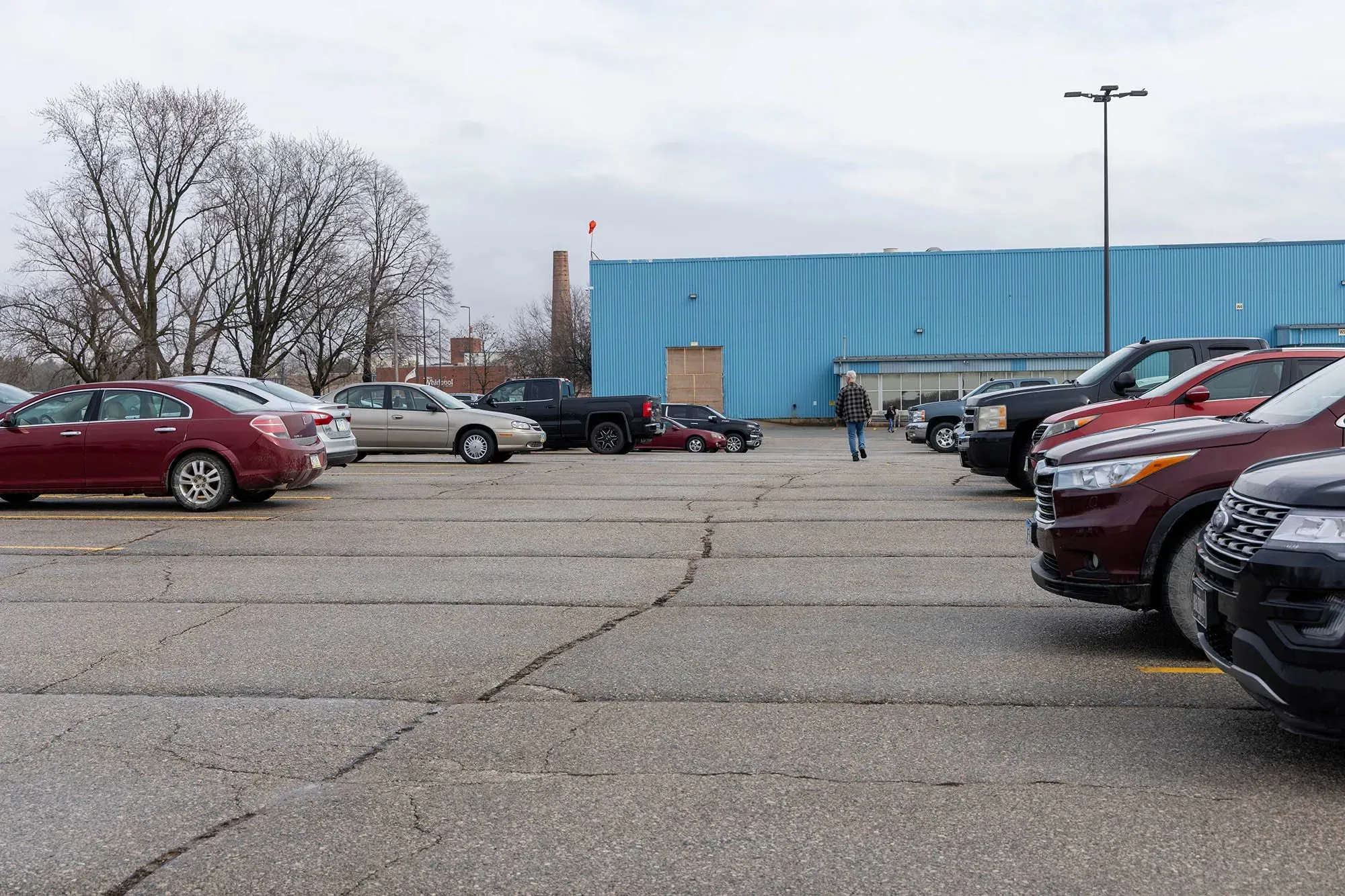موقف سيارات فارغ أمام مصنع ويرلبول في أمانة، أيوا، مع شخص يمشي نحو المبنى، مما يعكس تأثير تسريح العمال في الصناعة.
