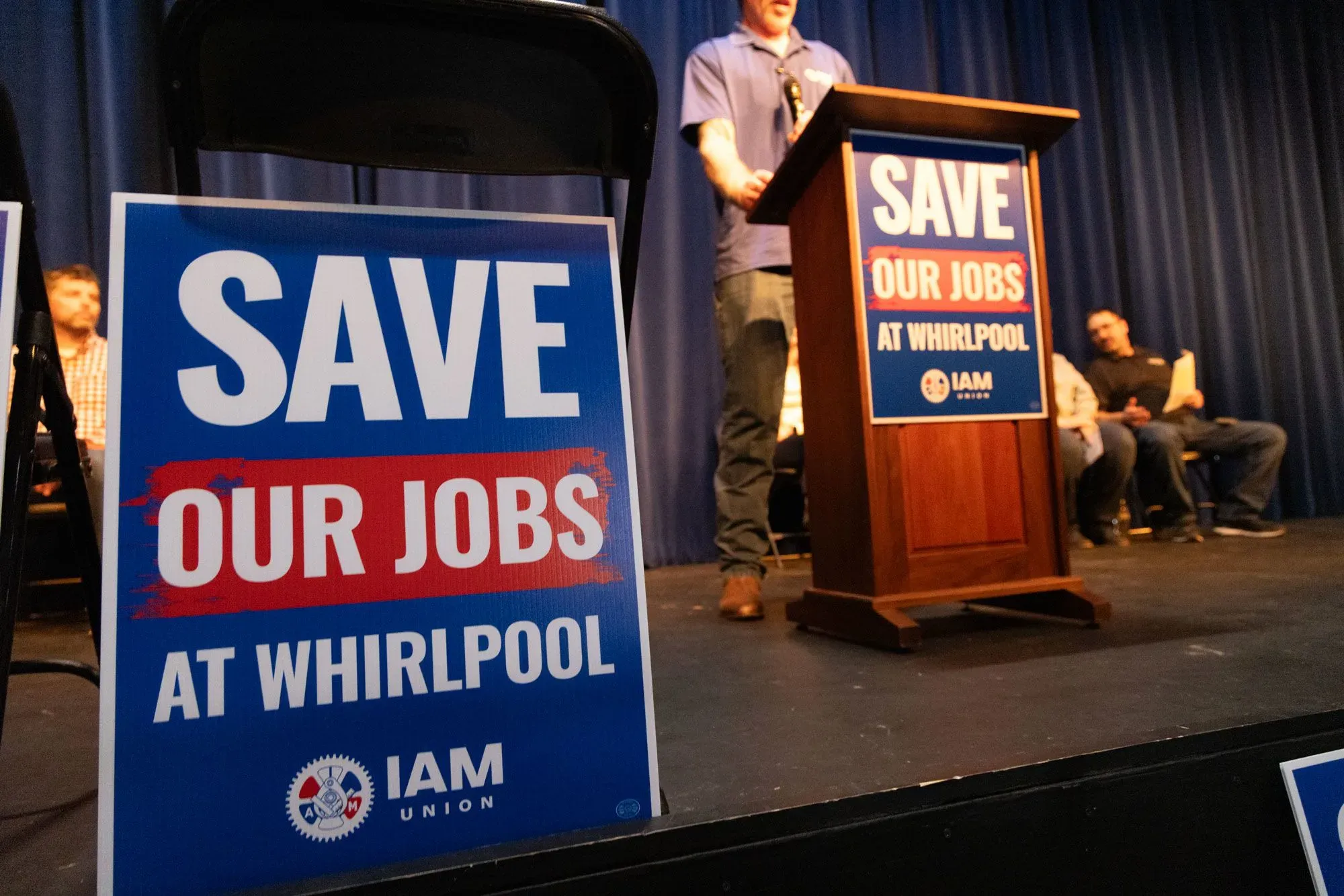 لافتة كبيرة تحمل عبارة "أنقذوا وظائفنا في ويرلبول" خلال حدث نقابي، تعكس القلق بشأن تسريح العمال في صناعة الأجهزة.