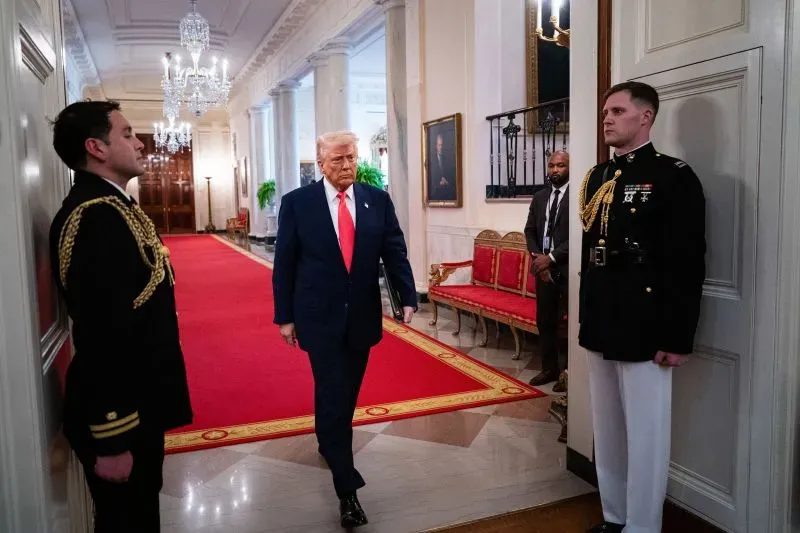 دونالد ترامب يمشي في الممر داخل البيت الأبيض، محاطًا بموظفين، في مشهد يعكس أجواء السلطة والتوتر خلال ولايته الثانية.