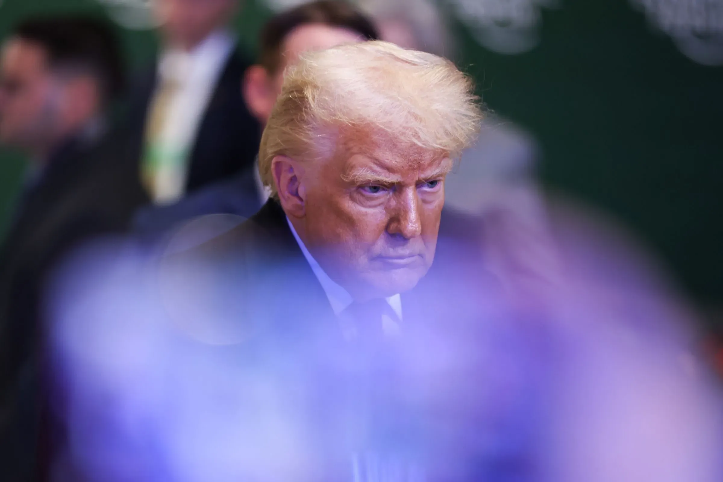 صورة لدونالد ترامب يظهر فيها بملامح جدية، محاطًا بأشخاص آخرين، تعكس أجواء مناقشات اقتصادية حول الذكاء الاصطناعي والنمو الاقتصادي.