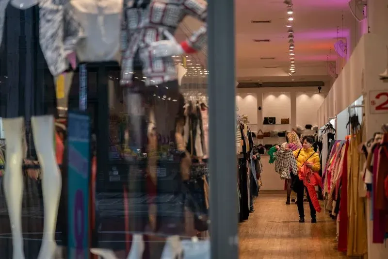 امرأة تتسوق في متجر ملابس، مع عرض لعدد من الملابس على الأرفف، تعكس حالة الاستهلاك في الاقتصاد الأمريكي المتراجع.
