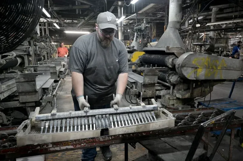 عامل في مطحنة فاريبولت يقوم بتركيب المعدات لصناعة البطانيات، مع وجود آلات تقليدية وحديثة في الخلفية.