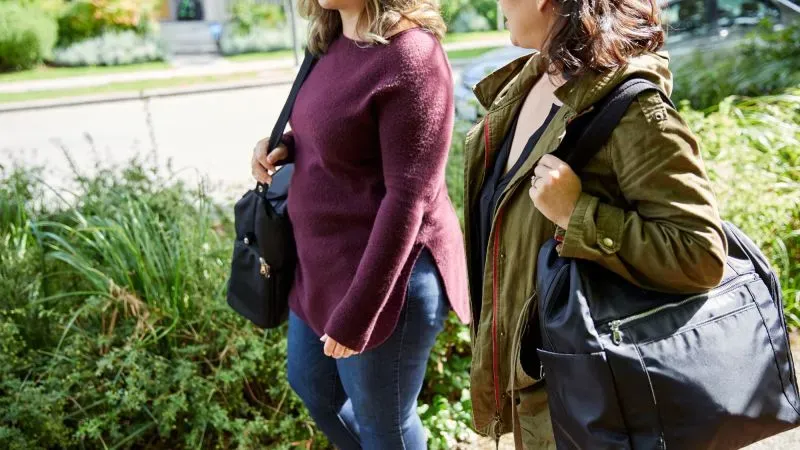 امرأتان تسيران معًا في حديقة، تحمل كل منهما حقيبة ظهر. تعكس الصورة تأثير الرسوم الجمركية على خيارات المستهلكين.