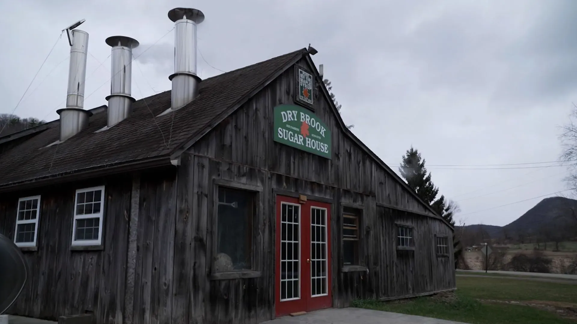 منزل دراي بروك للسكر في نيويورك، مع مدخنة معدنية، حيث يتم إنتاج شراب القيقب وسط غابات القيقب خلال موسم القيقب.