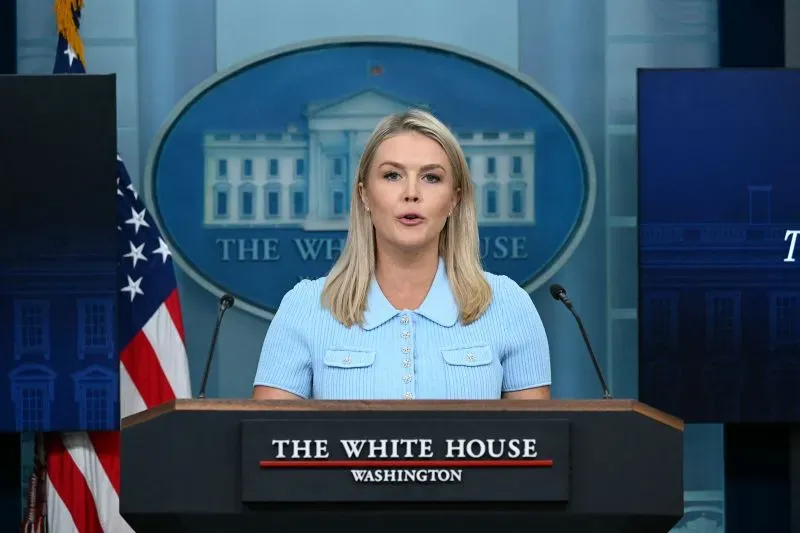 متحدثة رسمية في البيت الأبيض تتحدث أمام المنصة، مع العلم الأمريكي في الخلفية، تعكس الأجواء السياسية الحالية حول قضايا الهجرة.