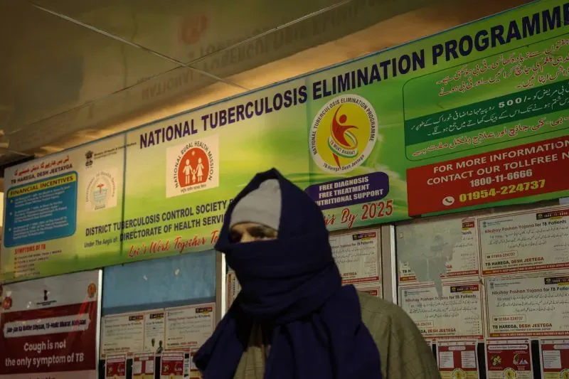 شخص يرتدي غطاء رأس يقف أمام لافتة كبيرة لبرنامج القضاء على السل الوطني، مع تفاصيل حول الدعم والعلاج المجاني.