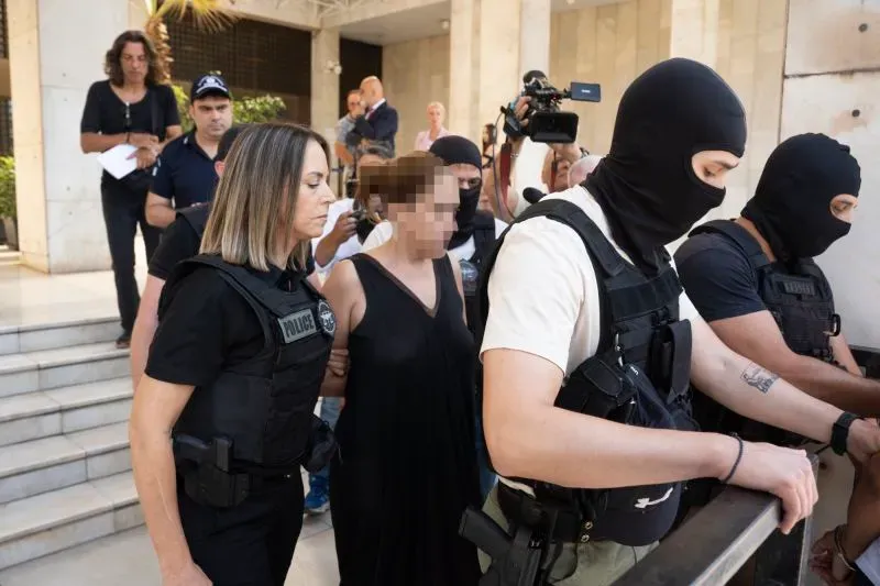 اعتقال امرأة ترتدي فستانًا أسود، محاطة برجال الشرطة الملثمين، في مشهد من أمام المحكمة، وسط تجمع للصحافة.