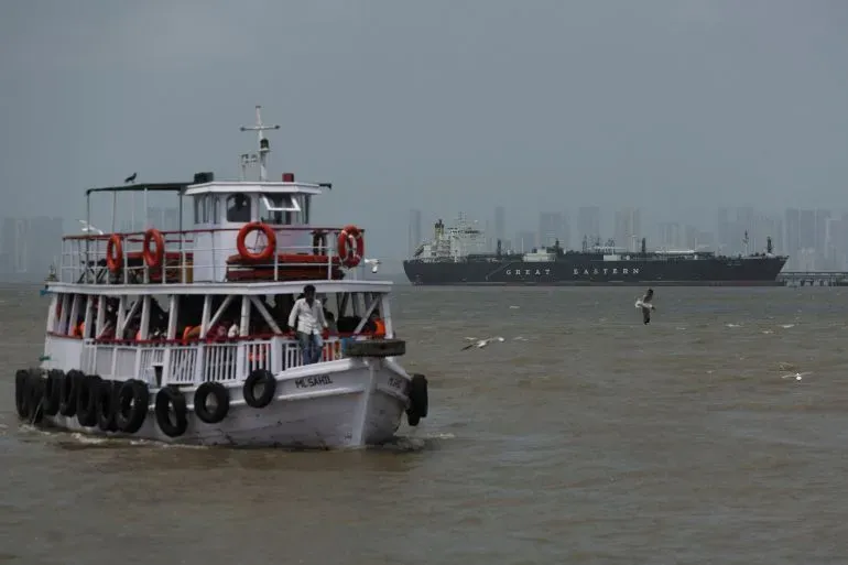 قارب صغير يبحر في المياه مع سفينة كبيرة في الخلفية، يمثل حركة الشحن الحيوية في مضيق هرمز وسط التوترات الإقليمية.