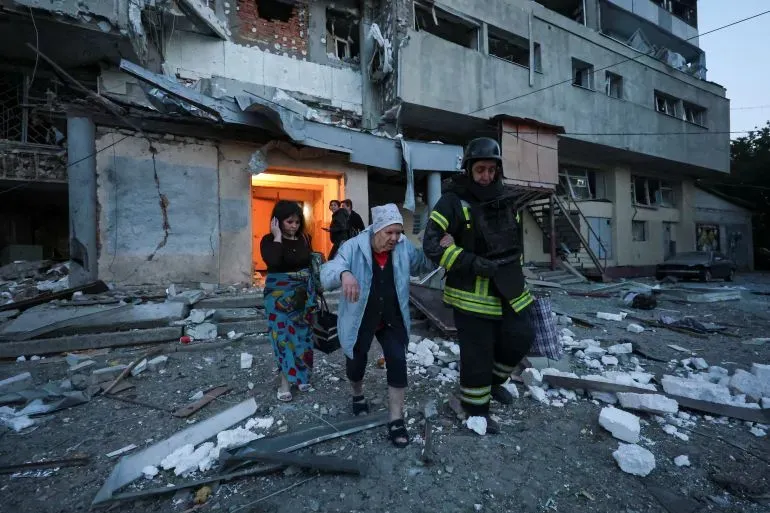 مدنيون يخرجون من مبنى سكني متضرر بعد غارة جوية في أوكرانيا، مع وجود حطام حولهم ودليل على الأضرار الكبيرة.