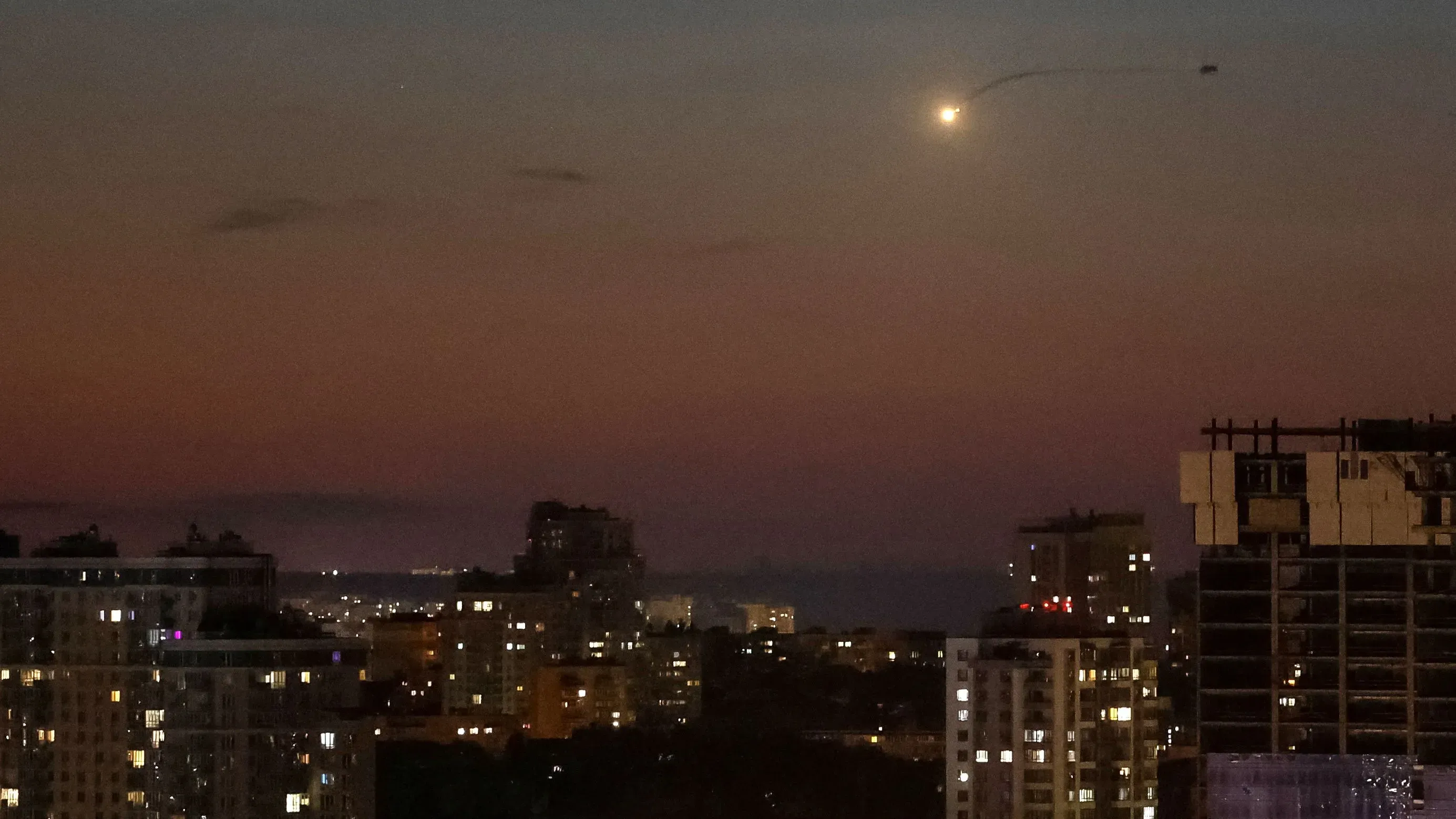 تظهر الصورة سماء الليل فوق مدينة أوكرانية، مع وميض ضوء يشير إلى هجوم جوي، وسط مبانٍ مضاءة في الأسفل.