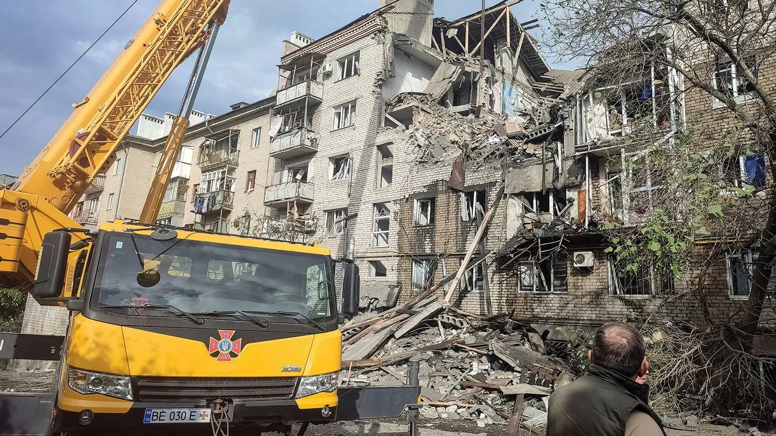 تظهر الصورة مبنى سكني مدمر جزئيًا جراء الهجمات الروسية، مع وجود رافعة إنقاذ في المقدمة، مما يعكس تأثير الصراع في أوكرانيا.