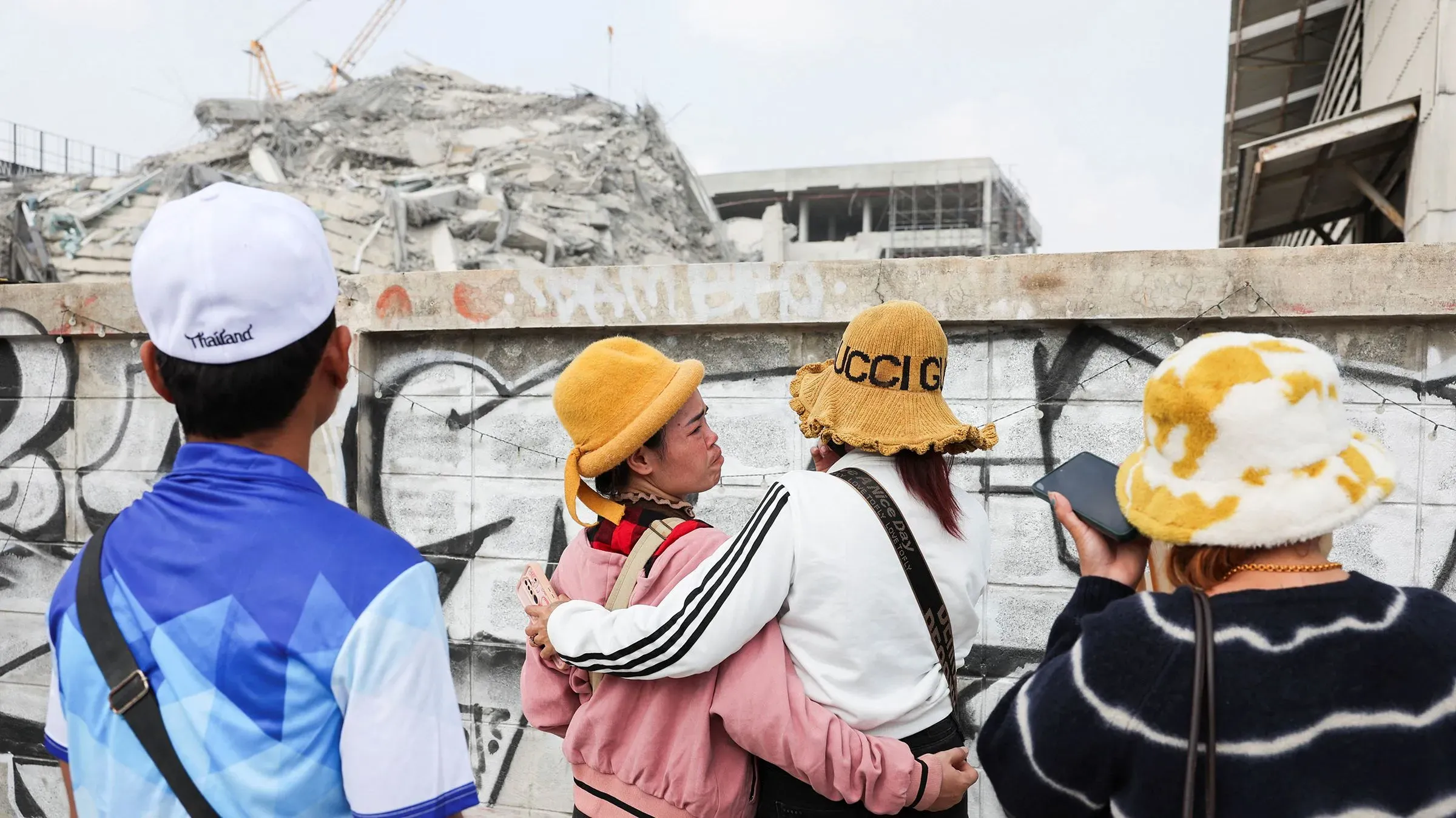 أحباء يراقبون أنقاض ناطحة سحاب تحت الإنشاء في بانكوك بعد زلزال قوي، مع مشاعر القلق والانتظار للعثور على المفقودين.