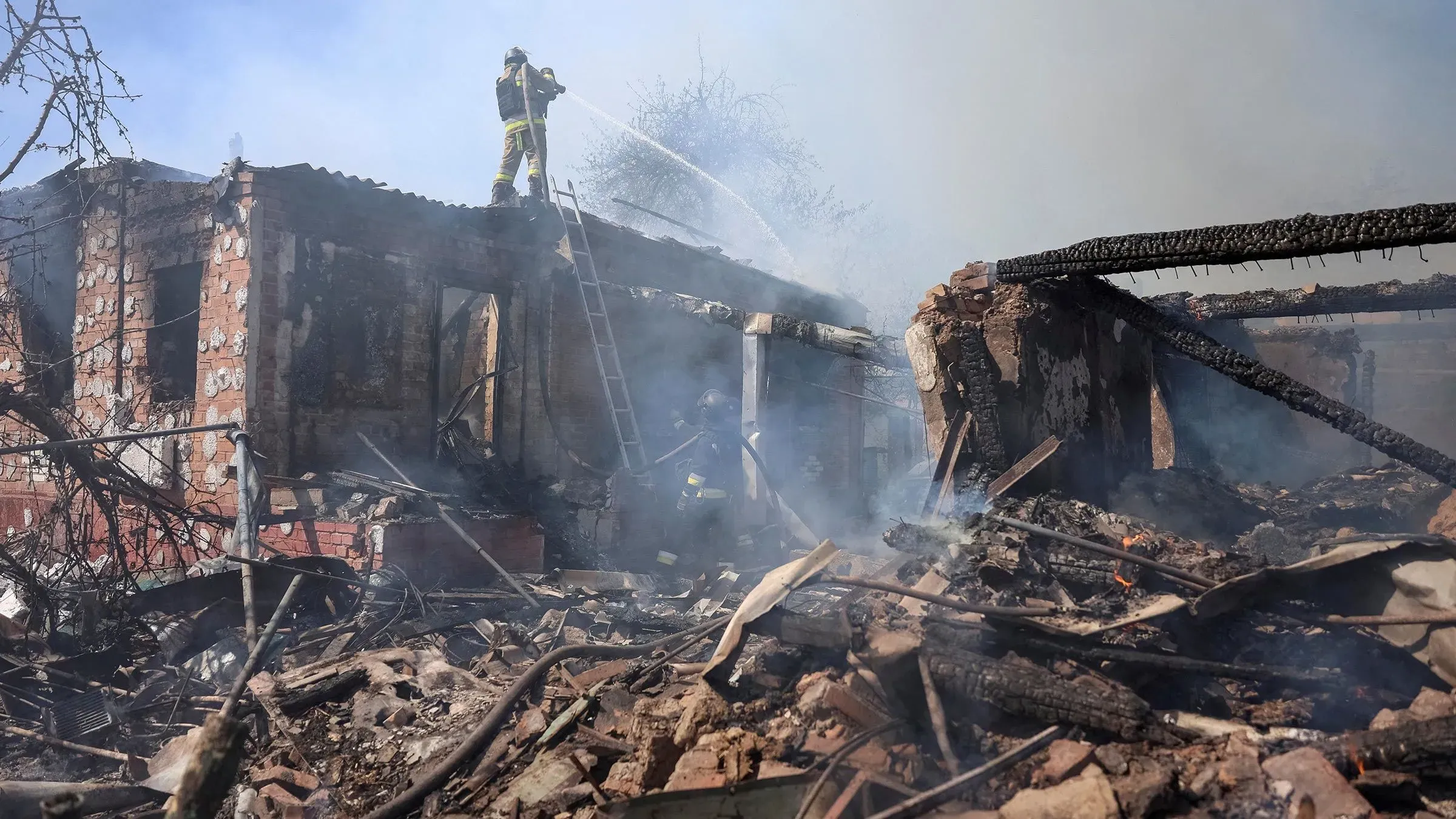 رجال الإطفاء يطفئون النيران في مبنى مدمر وسط الدخان، مما يعكس آثار الحرب الأوكرانية والدمار الناتج عنها.