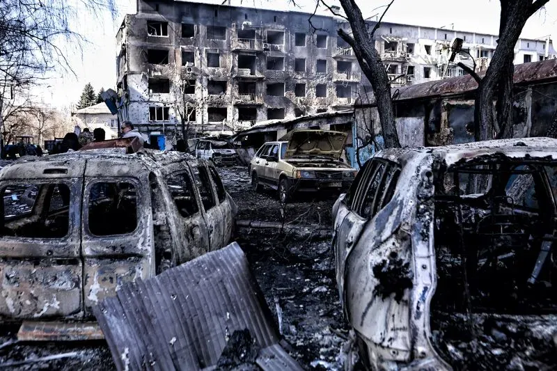 تظهر الصورة مشهدًا مدمرًا في أوكرانيا، مع سيارات محترقة ومبنى متضرر، مما يعكس آثار النزاع المستمر والضغط الدولي لوقف إطلاق النار.