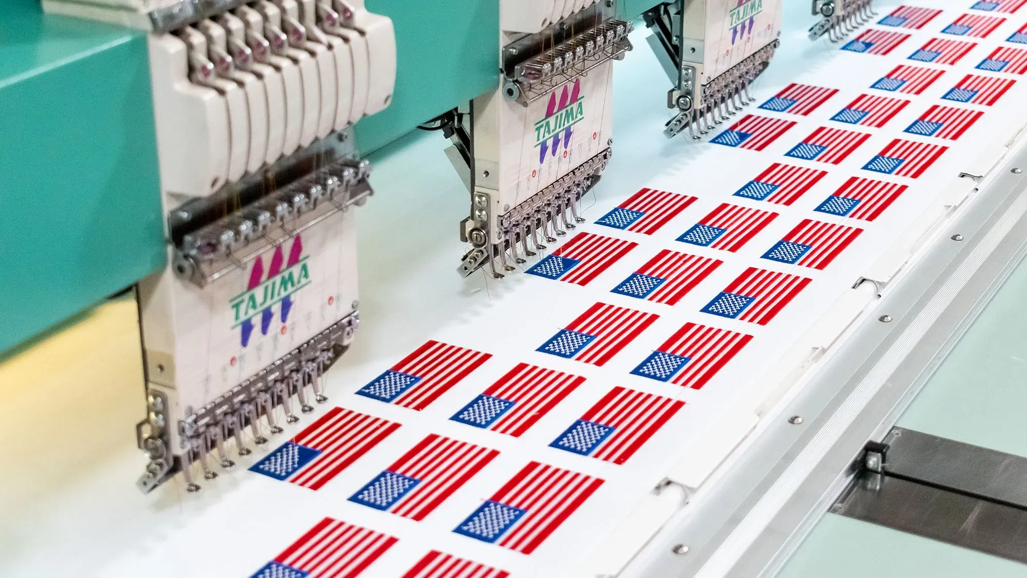 آلات تطريز تعمل على إنتاج علم الولايات المتحدة، تُظهر عملية التصنيع في شركة World Emblem، التي تنقل إنتاجها إلى جمهورية الدومينيكان.