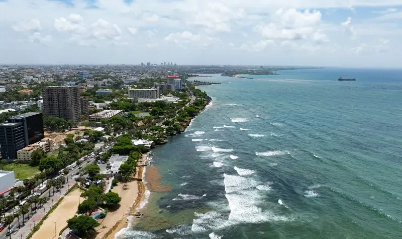 منظر جوي لجمهورية الدومينيكان يظهر الشاطئ والمباني السكنية، مع أمواج البحر في الخلفية، يعكس بيئة جذابة للاستثمار والتصنيع.