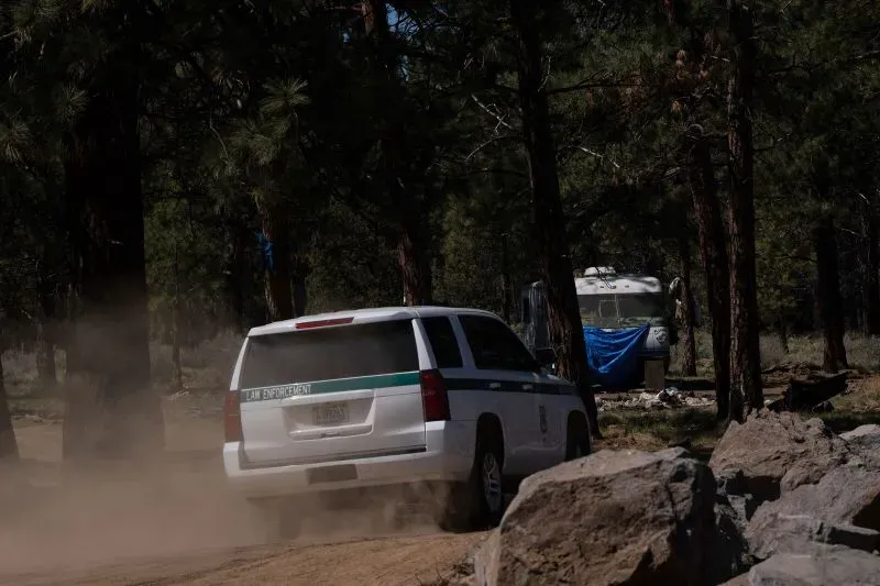 سيارة إنفاذ القانون تسير في غابة ديشوتس الوطنية، بالقرب من مخيم للمشردين، وسط أشجار الصنوبر والغبار.