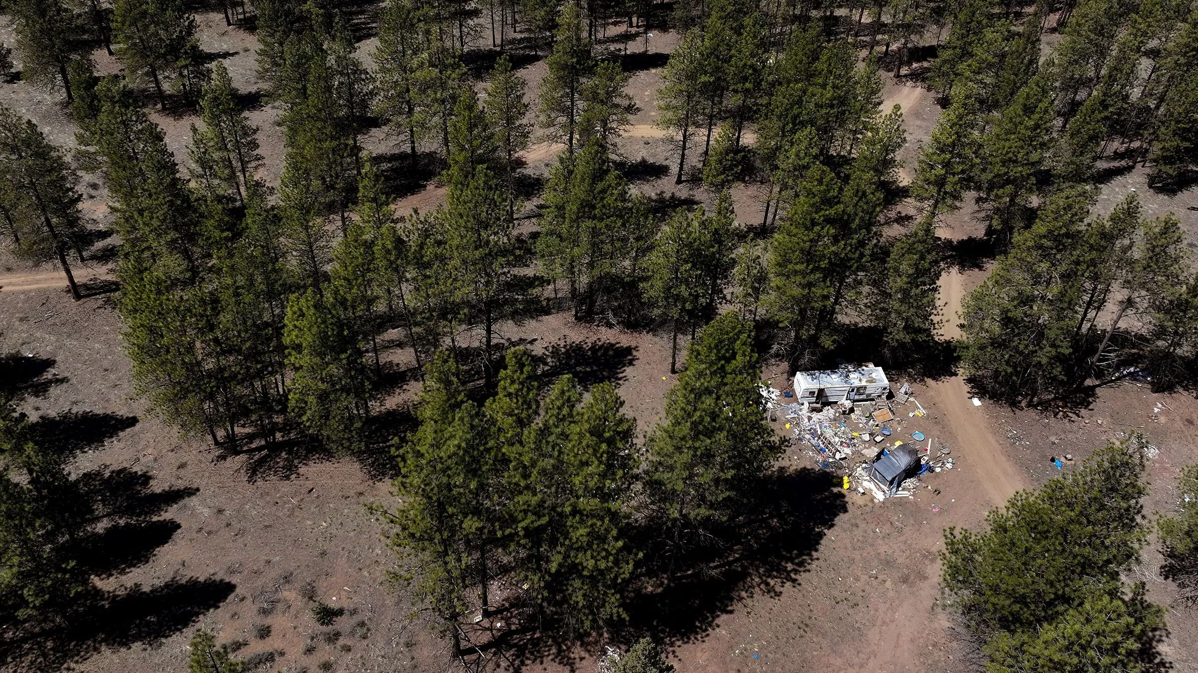 مخيم مؤقت وسط غابة ديشوتس الوطنية في أوريغون، يظهر المقطورات والأغراض المبعثرة، مع أشجار الصنوبر المحيطة، في سياق مشروع إدارة حرائق الغابات.