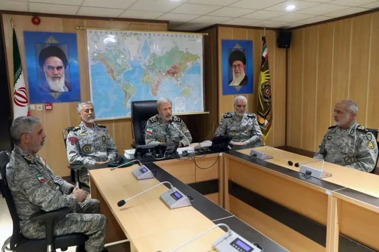 اجتماع عسكري في إيران، حيث يظهر عدد من الضباط العسكريين أمام خريطة العالم وصور لقادة إيرانيين، في سياق التوترات الإقليمية.