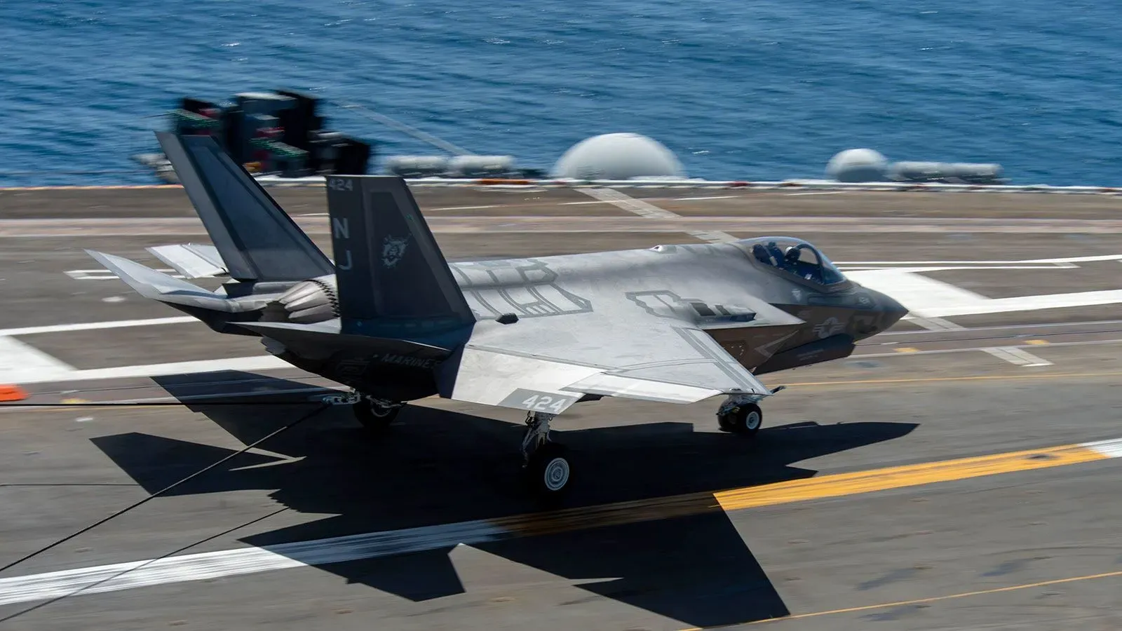 تحلق طائرة F-35 تابعة للبحرية الأمريكية فوق حاملة طائرات، مع عرض تفاصيلها المميزة وتصميمها المتقدم.