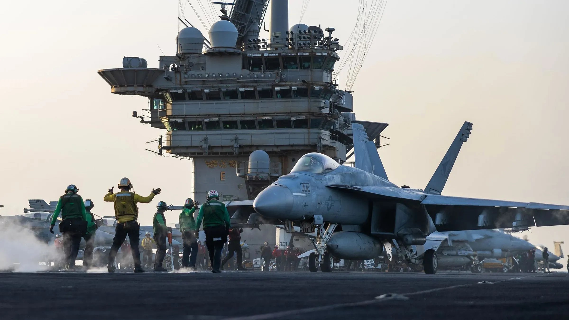 طائرة F/A-18 سوبر هورنيت على متن حاملة الطائرات هاري ترومان، مع طاقم بحري يعمل في الخلفية أثناء عمليات الصيانة.