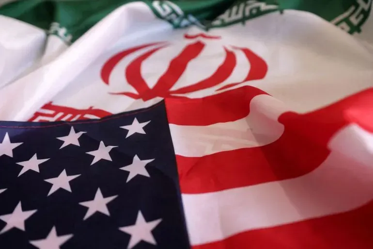 علم إيران يتداخل مع علم الولايات المتحدة، مما يرمز إلى التوترات بين البلدين في سياق العقوبات الأمريكية الجديدة على إيران.