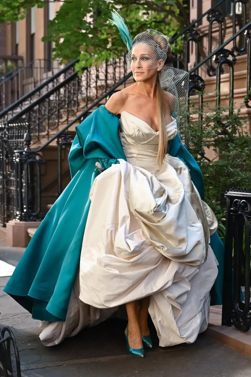 كاري برادشو ترتدي فستان زفاف فخم من تصميم فيفيان ويستوود، مع عباءة زرقاء وحذاء بكعب عالٍ، في مشهد درامي من مسلسل "الجنس والمدينة".