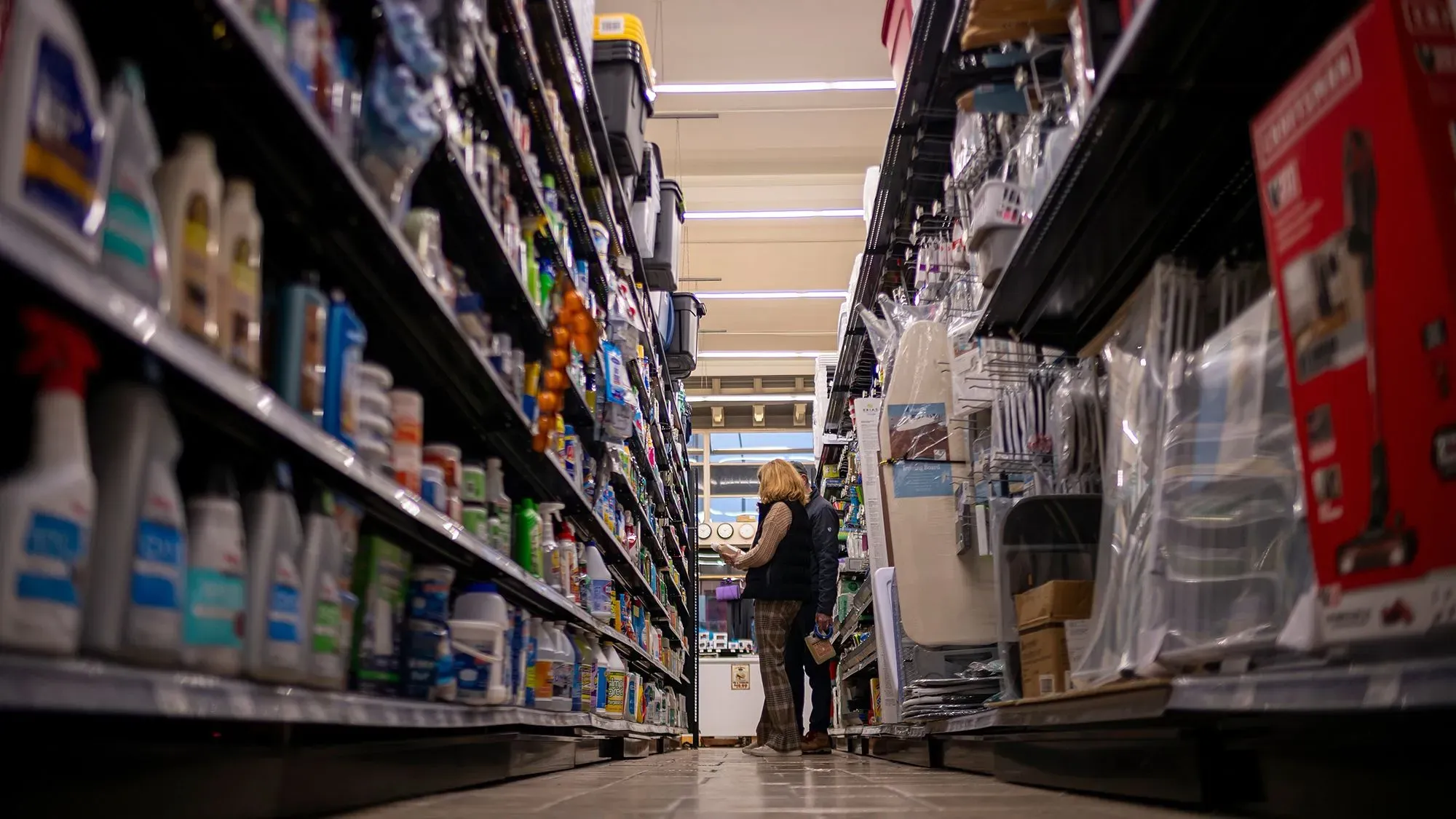 امرأة تتسوق في ممر متجر، محاطة بأرفف مليئة بالمنظفات والمنتجات المنزلية، في سياق الحديث عن المخاوف من الركود الاقتصادي.