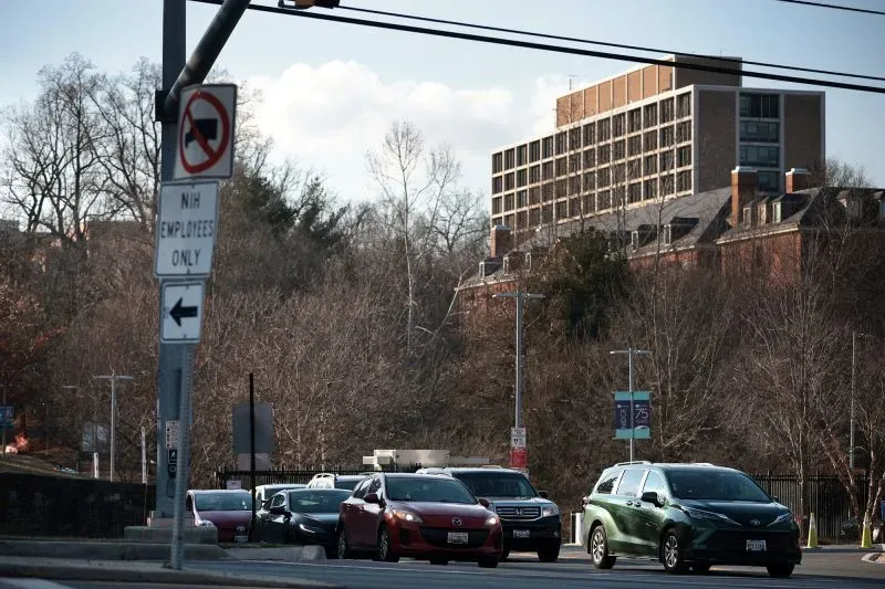 ازدحام مروري أمام مبنى حكومي، مع لافتات تشير إلى منطقة موظفي المعاهد الوطنية للصحة، تعكس تأثير تسريح العمال في واشنطن.