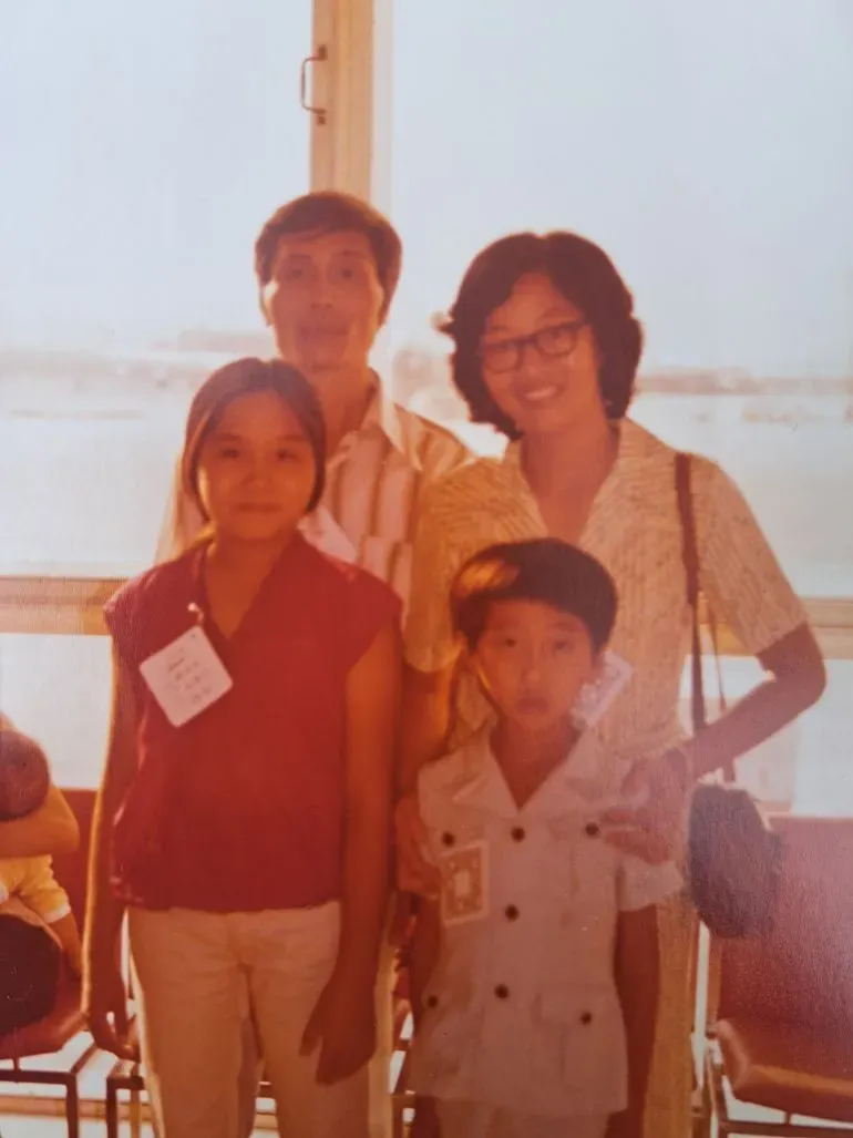 عائلة فيتنامية مكونة من أربعة أفراد، تضم والدين وطفلين، في مطار، تعبيرات وجوههم تعكس مشاعر الانتقال إلى ألمانيا الغربية.