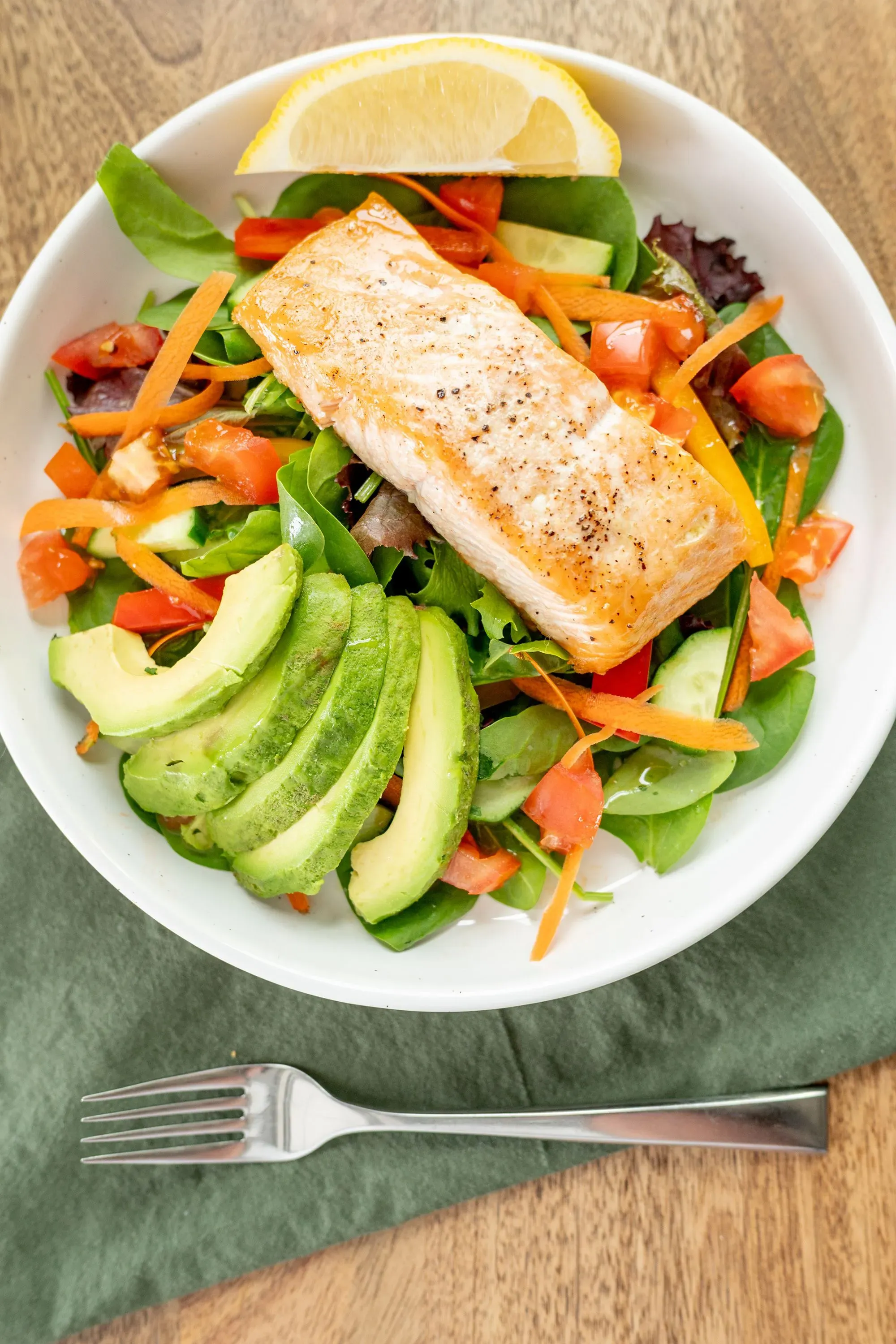 سلطة تحتوي على سمك السلمون المشوي، خضروات متنوعة مثل الأفوكادو والطماطم، مع شريحة ليمون، تعكس إرشادات الحمية الصحية.