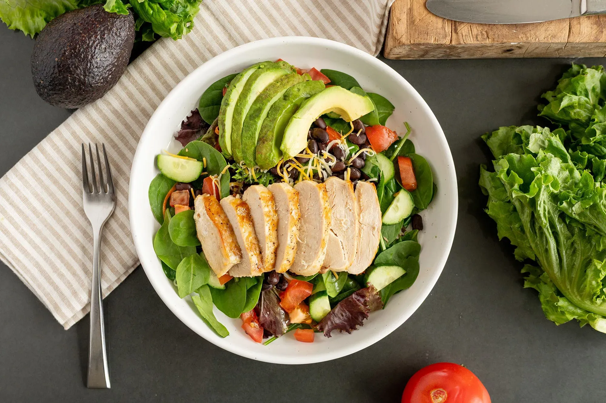 سلطة صحية تحتوي على قطع دجاج مشوي، أفوكادو، خضروات متنوعة مثل السبانخ والطماطم، مع شريحة من الخيار، تعكس إرشادات الحمية الغذائية.