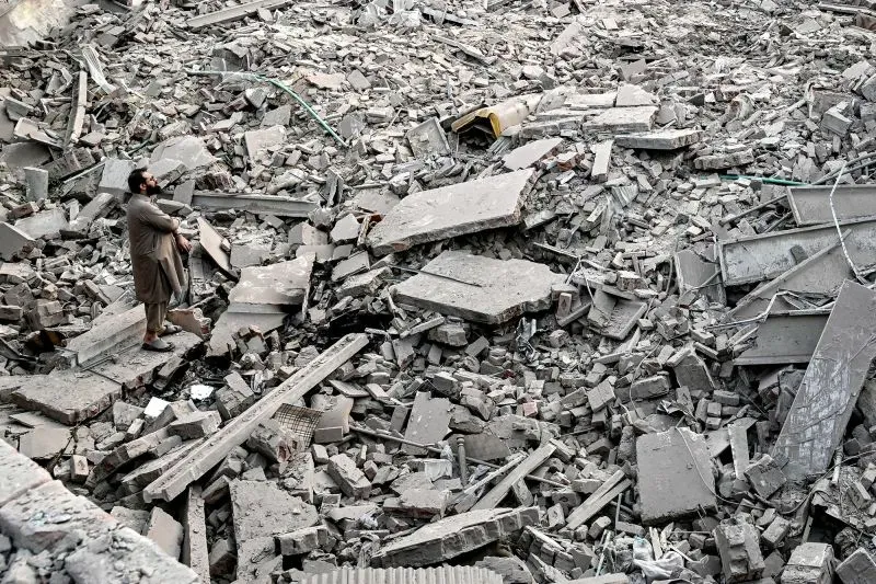 رجل يقف وسط أنقاض مبنى مدمر، تعكس الفوضى والدمار الناتج عن القتال بين الهند وباكستان في كشمير.